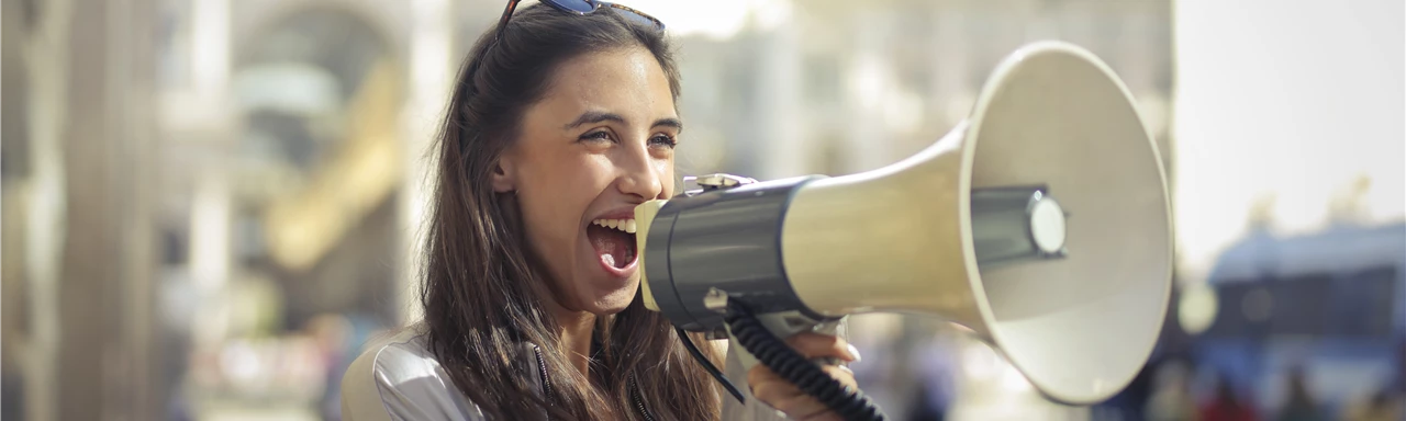 Cheerful young woman screaming into megaphone