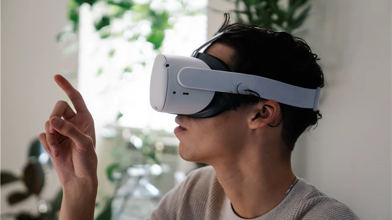 Side view of concentrated young guy in casual clothes experiencing virtual reality in modern headset at home