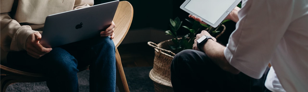 Photo of Couple Talking While Holding Laptop and Ipad